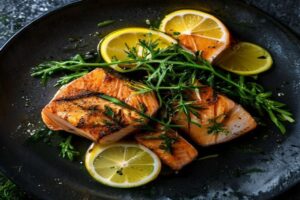 Keto Lachs mit Zitronenbutter und gerosetetem gruenem Spargel auf dunklem Teller