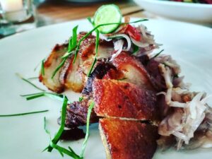 Knuspriger Keto Krustenbraten mit Schweinebauch auf weißem Teller mit Kräutern